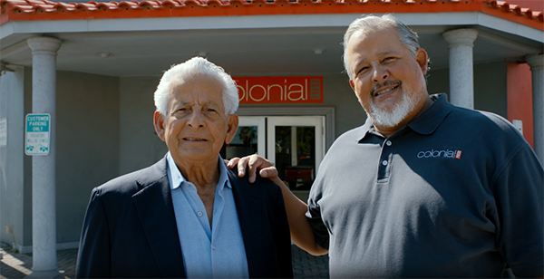 Two elderly gentlemen with grey hair from Colonial Press stand outside of their workplace.