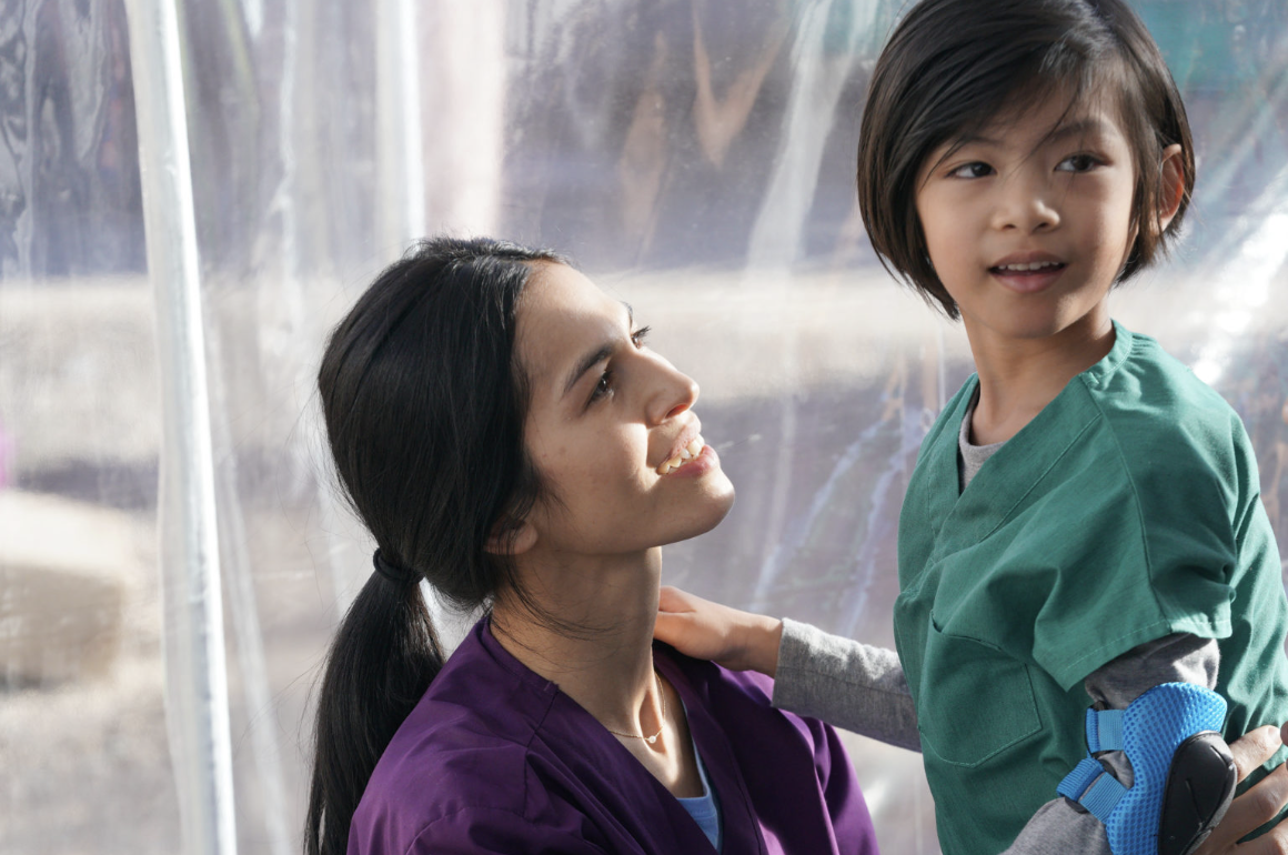 A women wearing purple scrubs is looking up and a young boy wearing green scrubs.