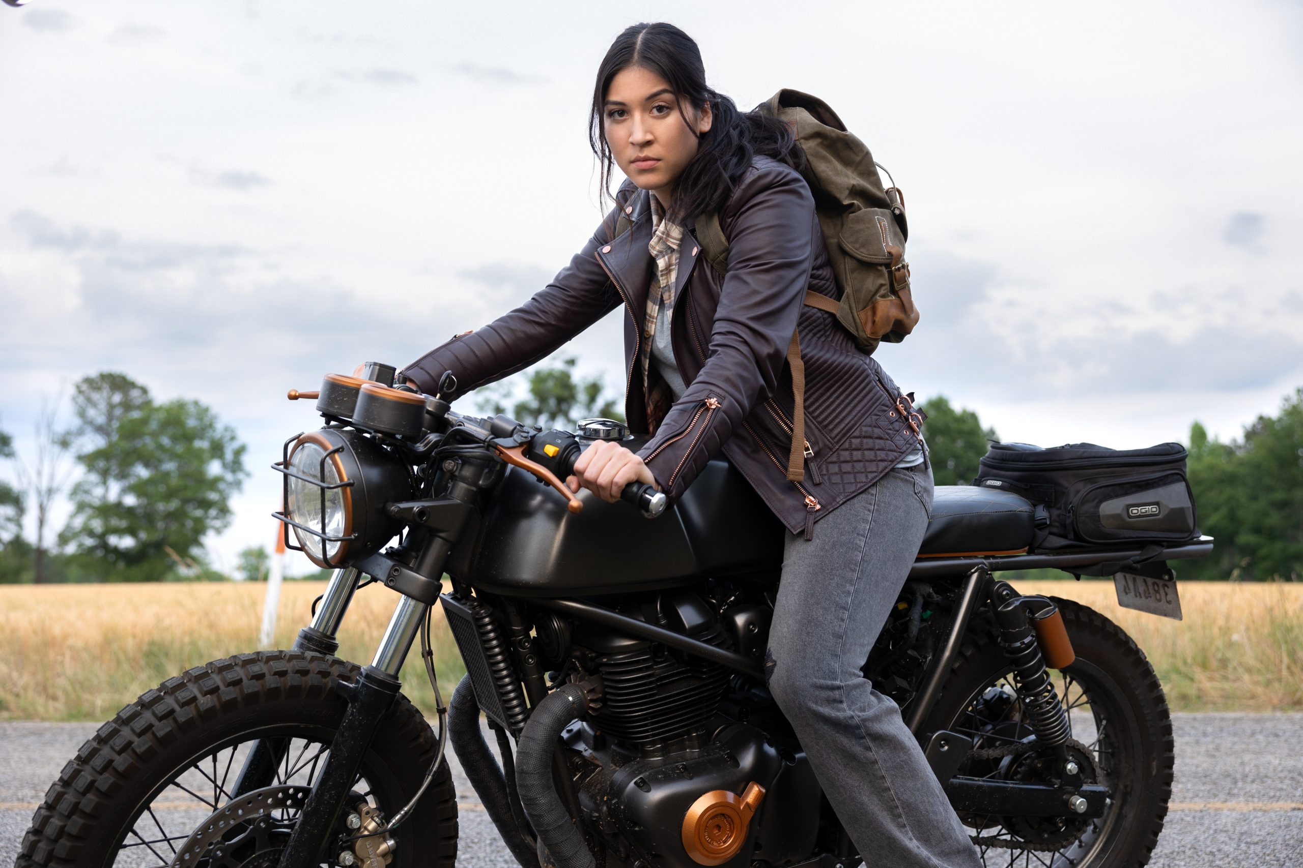 Alaqua Cox as Maya Lopez in Marvel Studios' Echo, exclusively on Disney+. Maya is sitting outside on her black motorcycle wearing a leather jacket, jeans and a backpack with part of her hair pulled back.